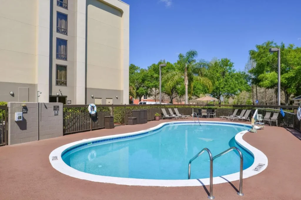 Kidney-shaped outdoor pool with loungers beside the Hampton Inn Closest to Universal Orlando building