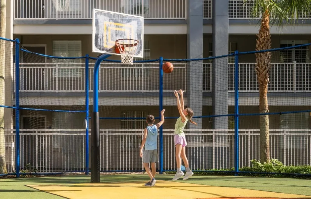 Ni&ntilde;os disparando aros en la cancha de baloncesto al aire libre cercada en Holiday Inn Resort Orlando Suites