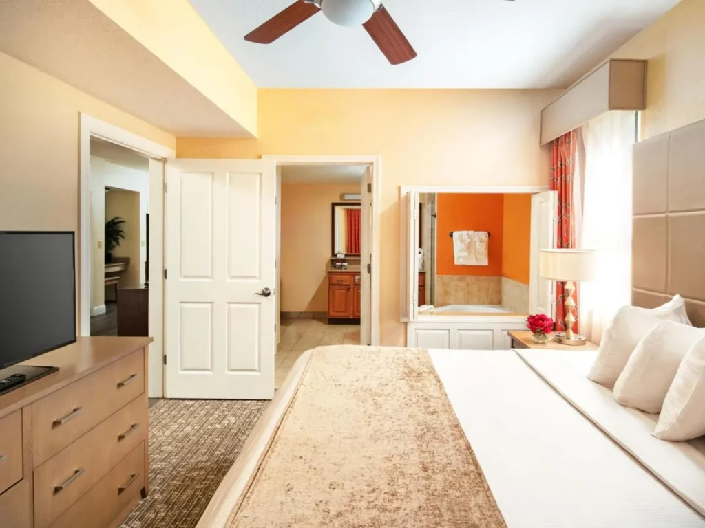 Dormitorio principal con cama king con una ventana interior a la ba&ntilde;era de hidromasaje en Floridays Resort Orlando