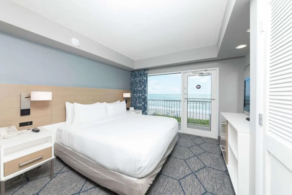 King bedroom with a balcony door opening toward the ocean at DoubleTree Suites Melbourne Beach