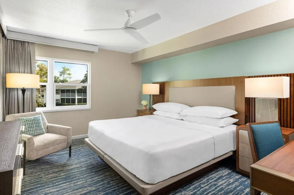 Dormitorio con cama king y pared con acento verde azulado, sillón y escritorio en una villa en Sheraton Vistana Resort