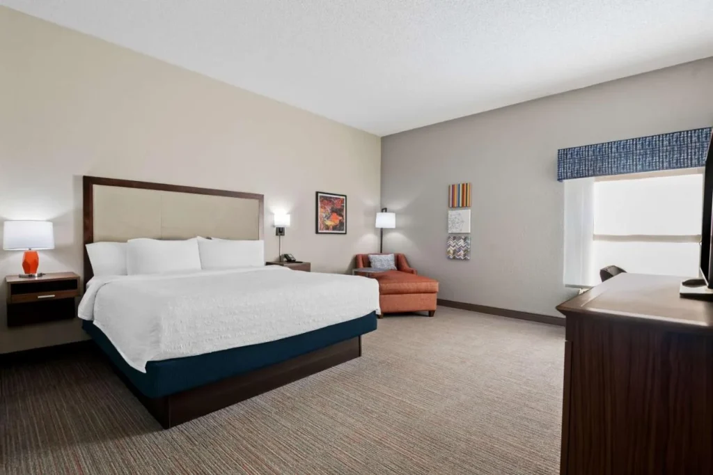 King guest room with a white bed and orange lounge chair at Hampton Inn Debary-Deltona