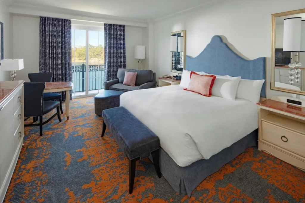 Habitación King con cabecera azul, sillón y puerta de balcón en el Loews Portofino Bay Hotel