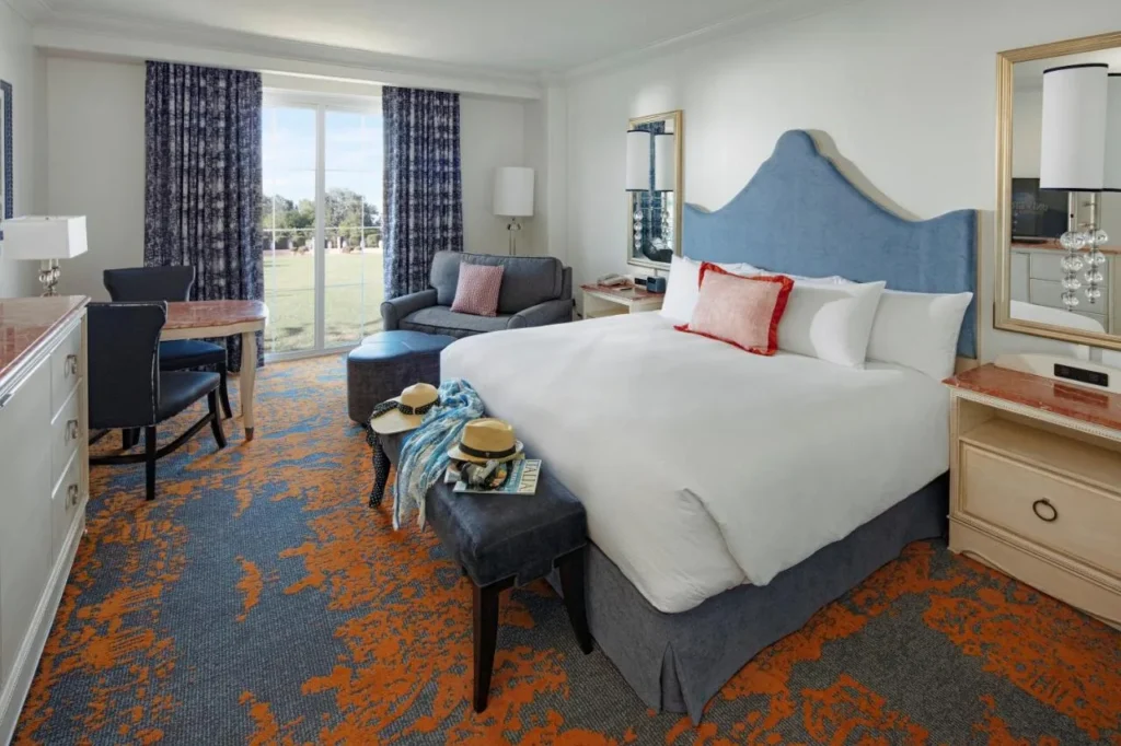 Habitación con cama king con cabecera azul, sofá y puertas con vistas al jardín en Loews Portofino Bay Hotel