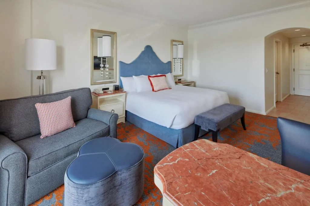King room with a blue headboard, sofa, ottoman and marble table at Loews Portofino Bay Hotel