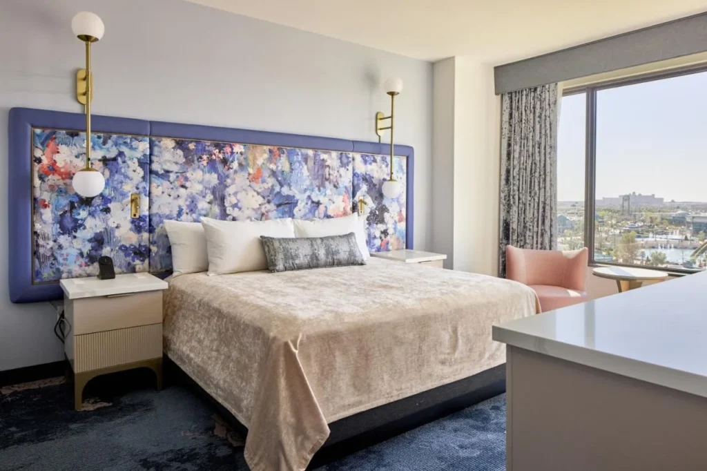 Habitación con cama king, cabecera floral, sillón rosa y ventana amplia en Universal Helios Grand Hotel
