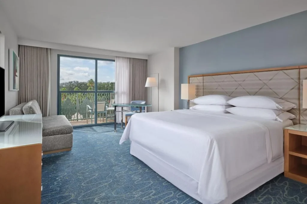 King room with a gray chaise, glass table and furnished balcony at Walt Disney World Dolphin