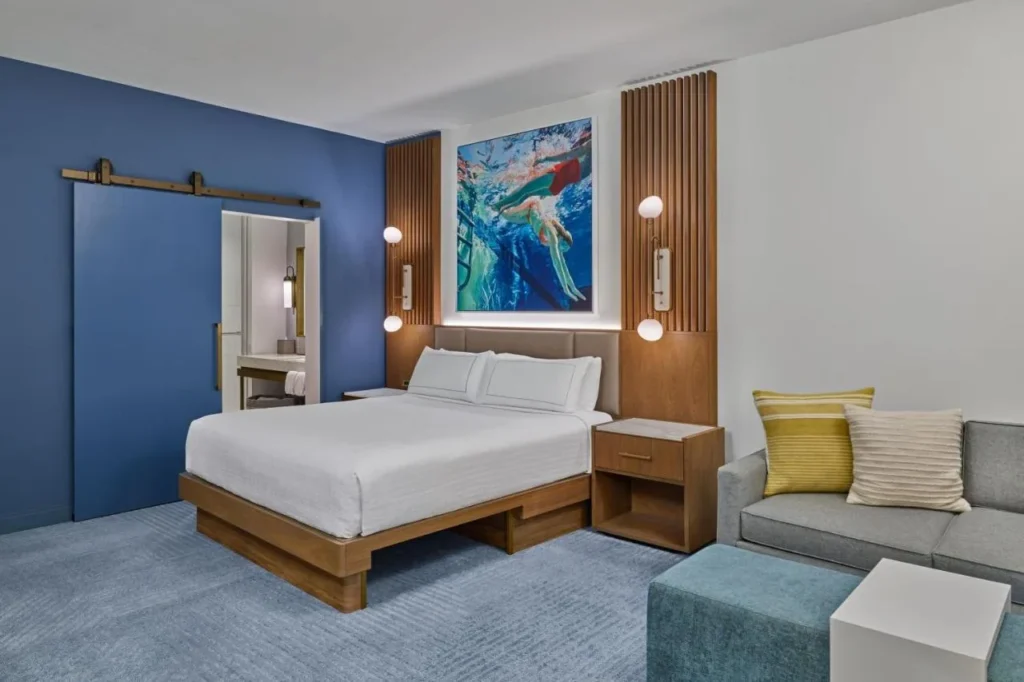 King room with blue barn door, swimmer painting and gray sofa, Walt Disney World Swan Reserve