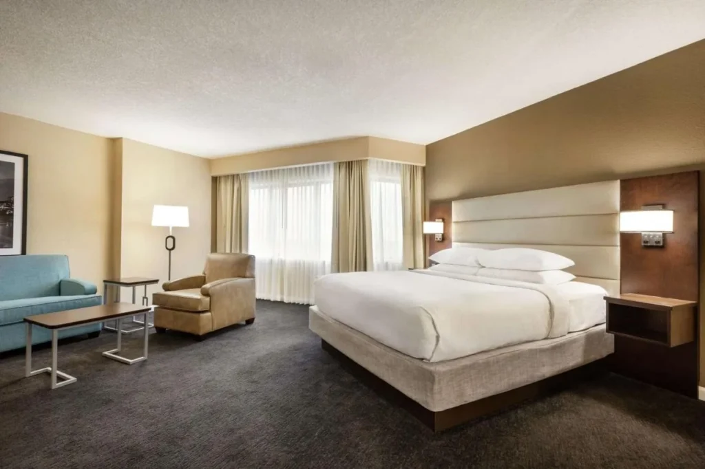 Habitaci&oacute;n con cama king y sof&aacute;, sill&oacute;n y cortinas transparentes en DoubleTree by Hilton Orlando Downtown