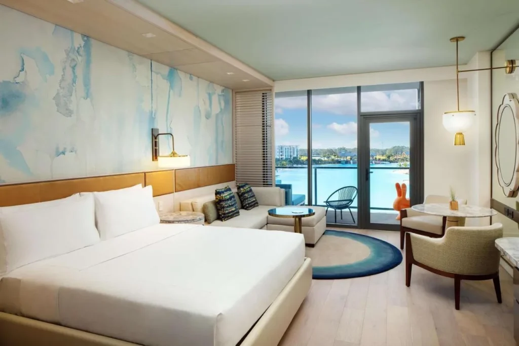 Habitación con cama king con sofá, pared de acuarela y balcón con vistas a la laguna en Conrad Orlando