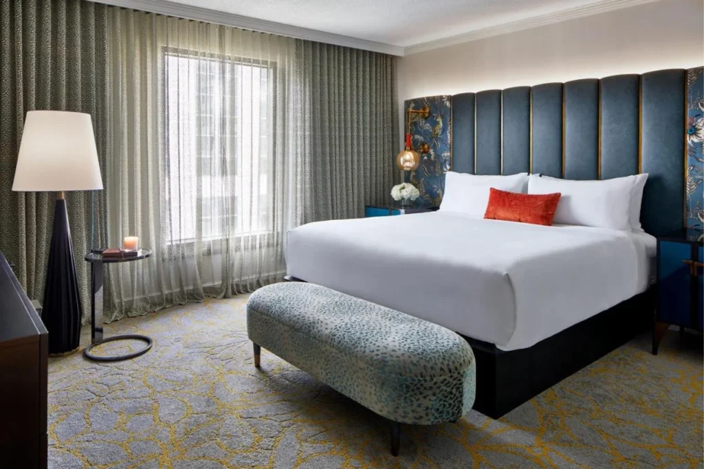 King room with a tall blue tufted headboard, upholstered bench and sheer curtains at Hotel Beauden