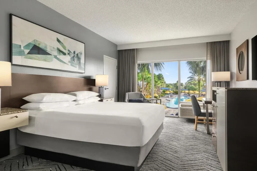 Habitaci&oacute;n King con ventana a la piscina y palmeras en Delta Hotels Orlando Celebration