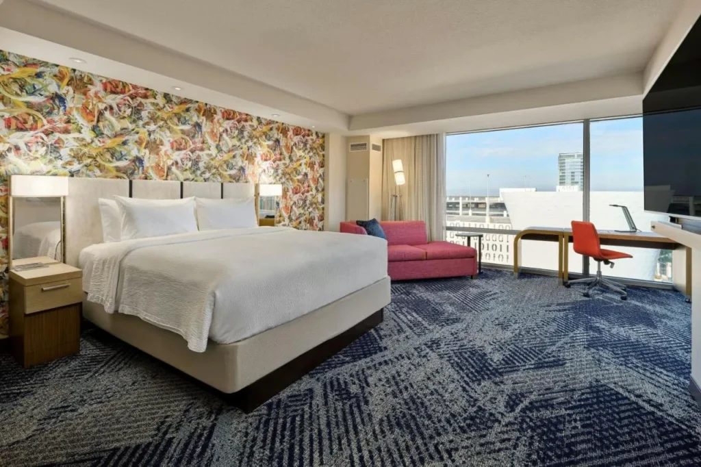 Habitaci&oacute;n King con pared floral abstracta, sof&aacute; rojo y ventana con vista a la ciudad en Courtyard Orlando Lake Nona