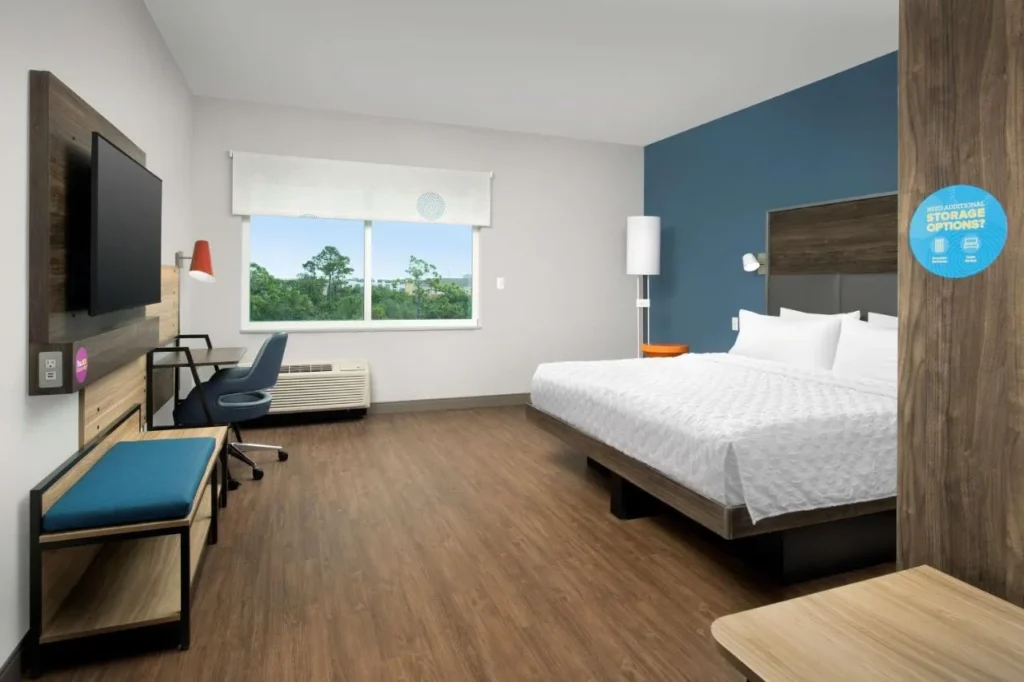 Habitaci&oacute;n con cama king y pared con acento azul, escritorio y banco en Tru by Hilton Orlando Convention Center