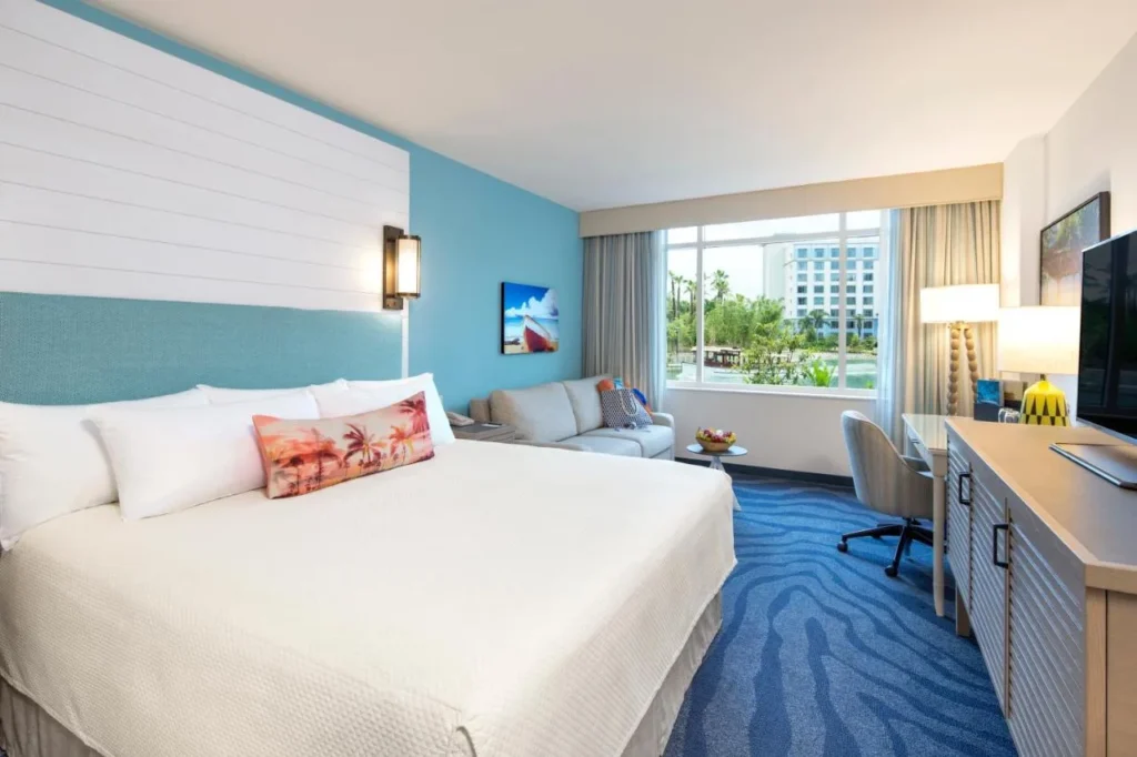 Habitación con cama king con detalles en azul, sofá y ventana grande en Loews Sapphire Falls Resort