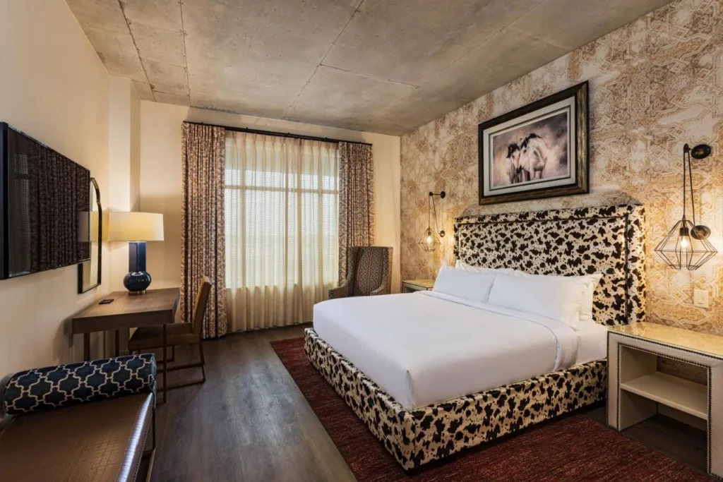 Habitaci&oacute;n con cama king y cabecero con estampado de piel de vaca, escritorio y papel pintado estampado en The Brownwood Hotel & Spa