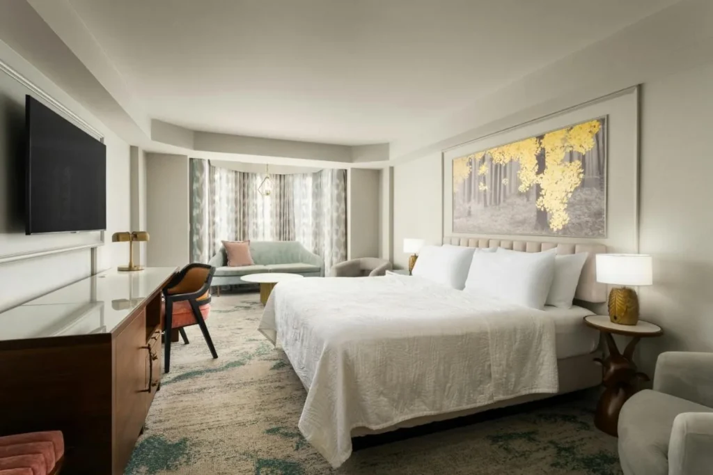 Habitaci&oacute;n con cama king con ilustraciones de &aacute;rboles dorados, sof&aacute; y escritorio en Castle Hotel, Autograph Collection