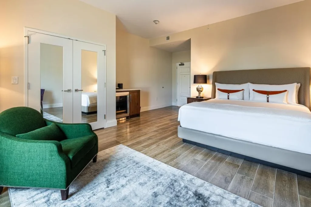Habitaci&oacute;n king con sill&oacute;n verde, suelo de madera y puertas de armario con espejos en The Riding Academy Hotel