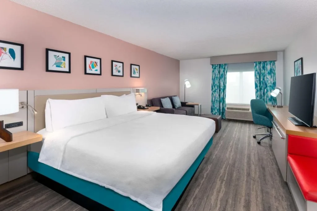 King room with pink accent wall, sofa and desk at Hilton Garden Inn I-Drive North