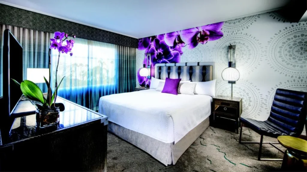Habitación King con mural de orquídea púrpura, cama blanca y sillón en Loews Royal Pacific Resort