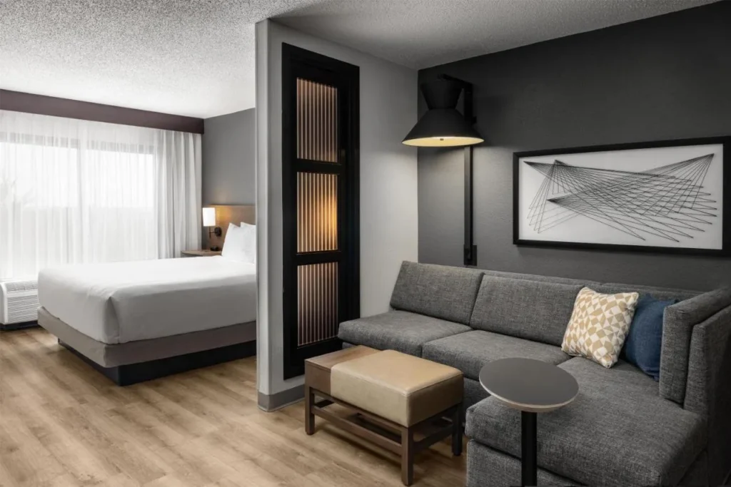 Habitaci&oacute;n con cama king con sof&aacute; seccional, otomana y mesa auxiliar en el Hyatt Place Orlando Airport