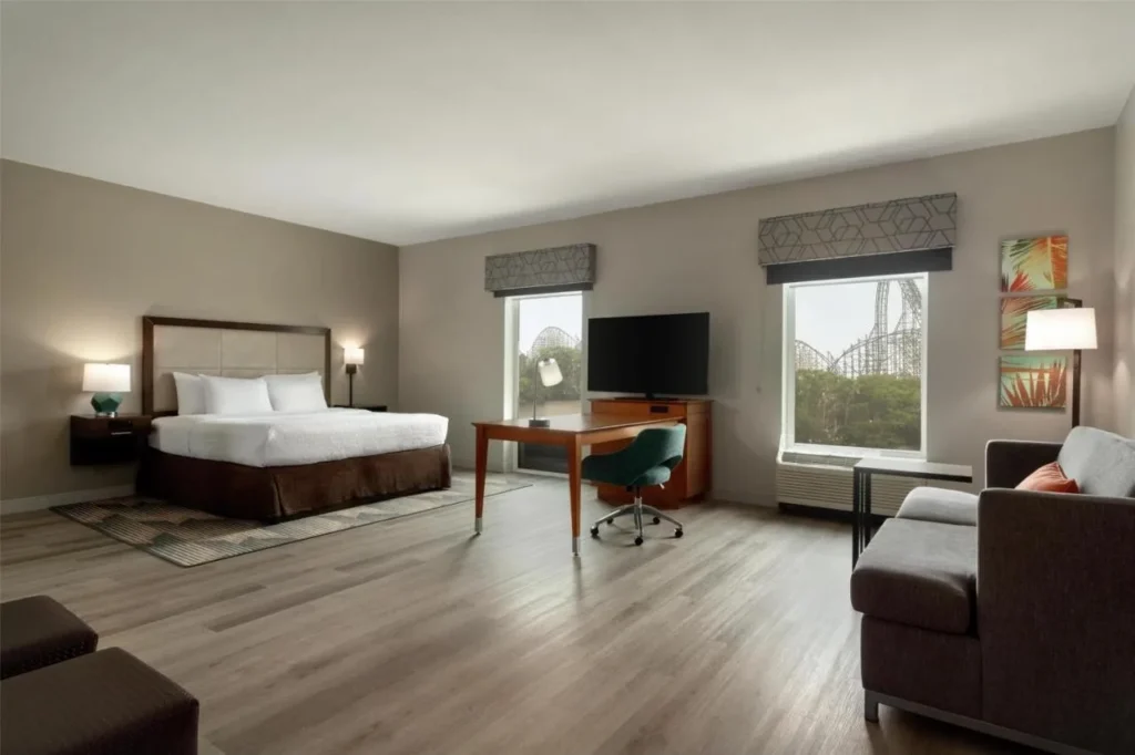 Habitación King con sofá y escritorio, pista de montaña rusa visible a través de las ventanas, Hampton Inn Busch Gardens