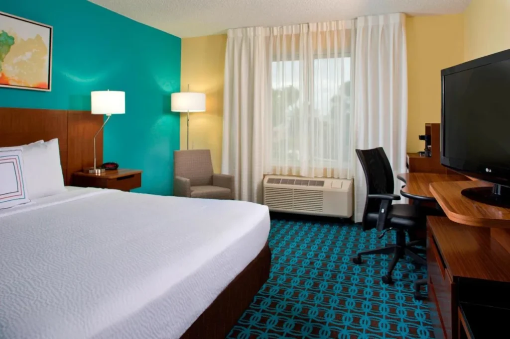 Habitaci&oacute;n con cama king y pared con acento verde azulado, escritorio y TV en Fairfield Inn & Suites Marriott Village