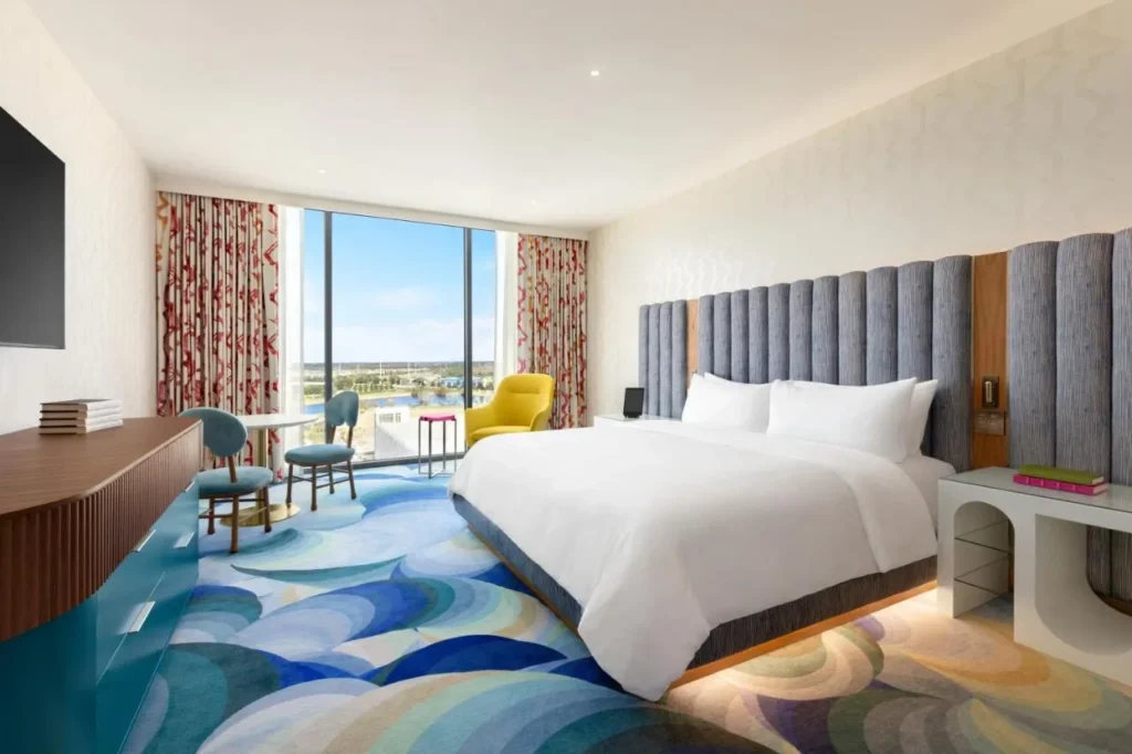 King room with wave-pattern carpet, yellow armchair and floor-to-ceiling window at Lake Nona Wave Hotel