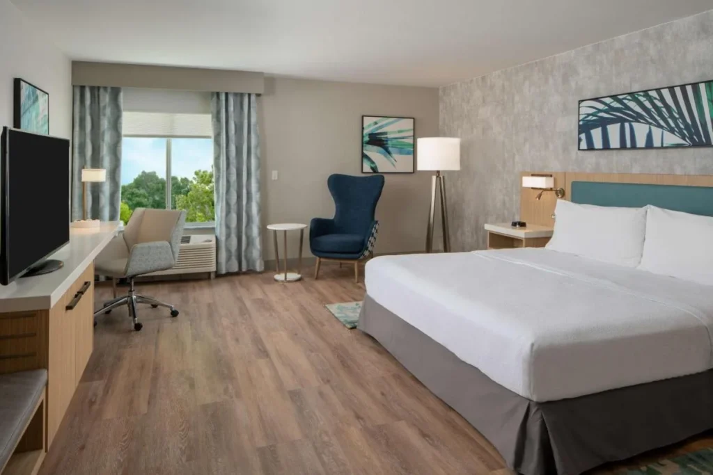Habitaci&oacute;n con cama king y suelo de madera, escritorio y sill&oacute;n azul en Hilton Garden Inn Orlando Airport