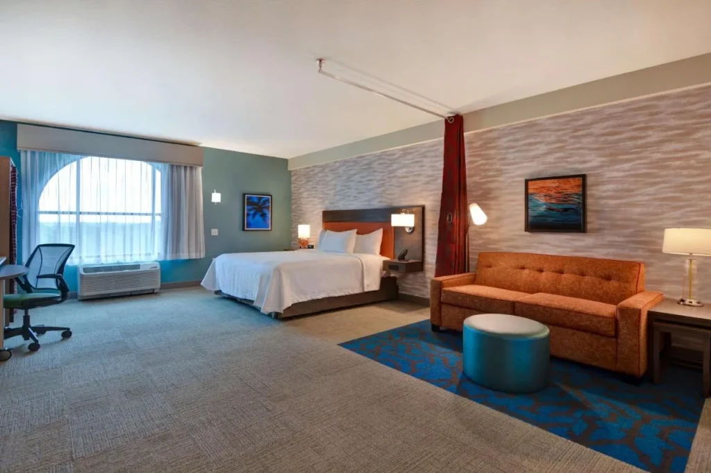 Estudio King con sof&aacute; naranja, escritorio y ventana arqueada en Home2 Suites Flamingo Crossings