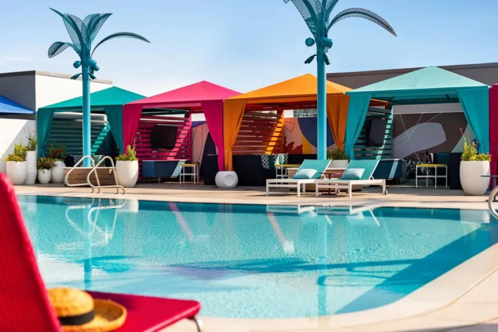 Piscina en la azotea del Lake Nona Wave Hotel con coloridas cabañas con cortinas y luces esculpidas de palmeras