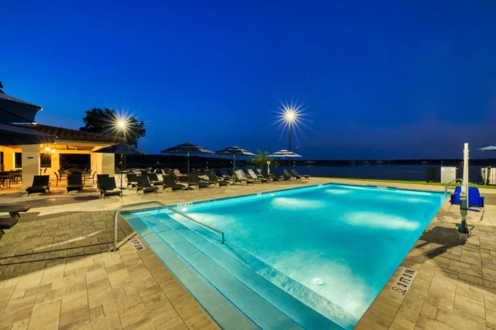 Piscina frente al lago iluminada por la noche con tumbonas y sombrillas en Siena en Bella Collina en Montverde