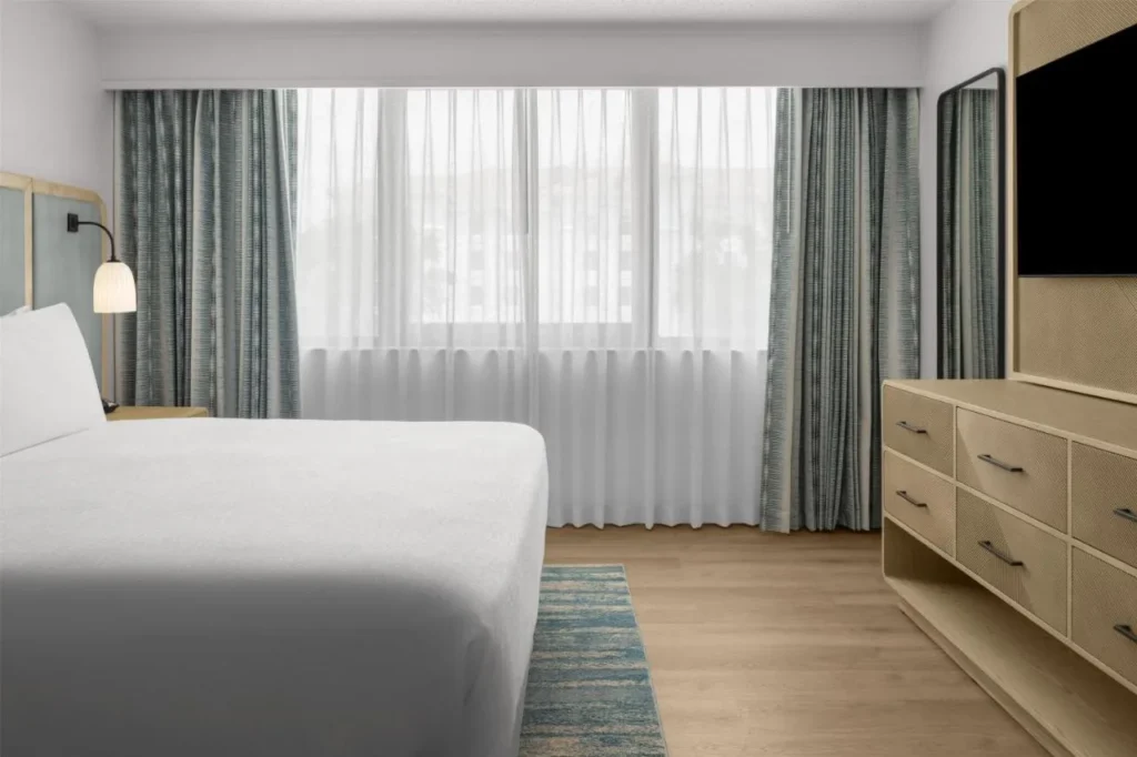 Cama grande, c&oacute;moda y TV de pared en un dormitorio suite renovado en Embassy Suites ICON Park