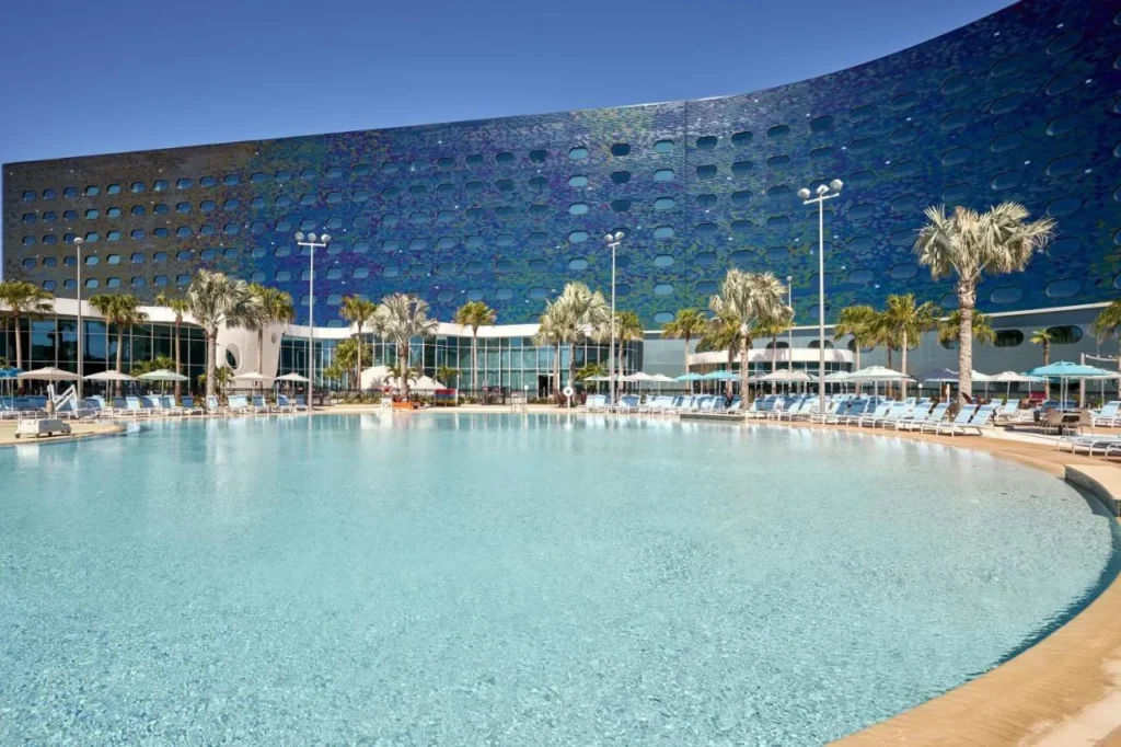 Gran piscina curva y tumbonas azules debajo de la torre de mosaico de Universal Terra Luna Resort