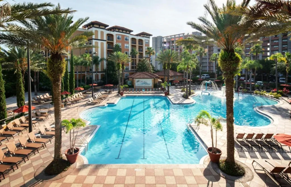 Gran piscina con palmeras, tumbonas y los edificios del complejo detr&aacute;s en Floridays Resort Orlando