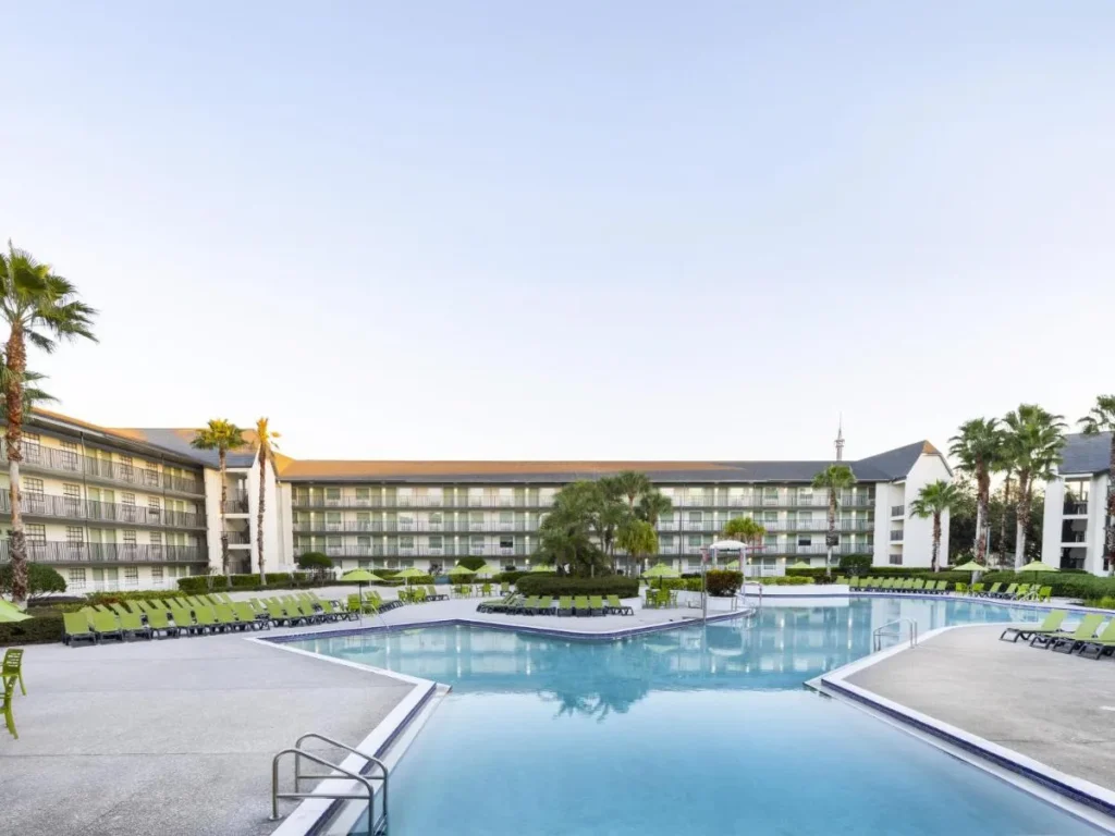 Large outdoor pool with green loungers in front of the guest wings at Avanti International Resort