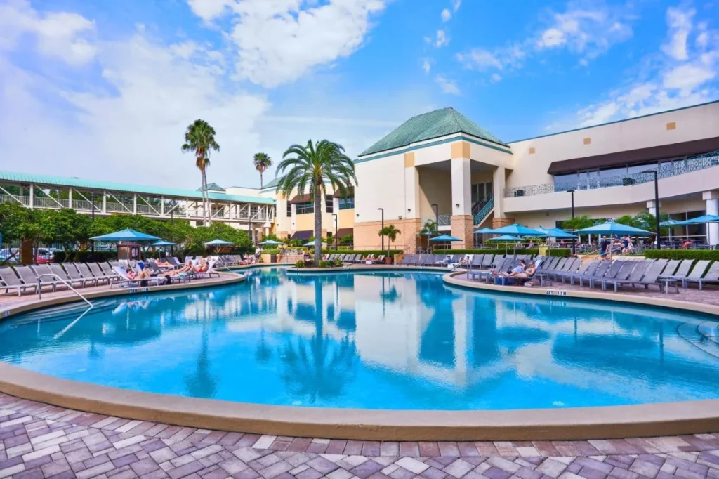 Large outdoor pool with loungers and palm trees beside the Rosen Plaza Hotel buildings