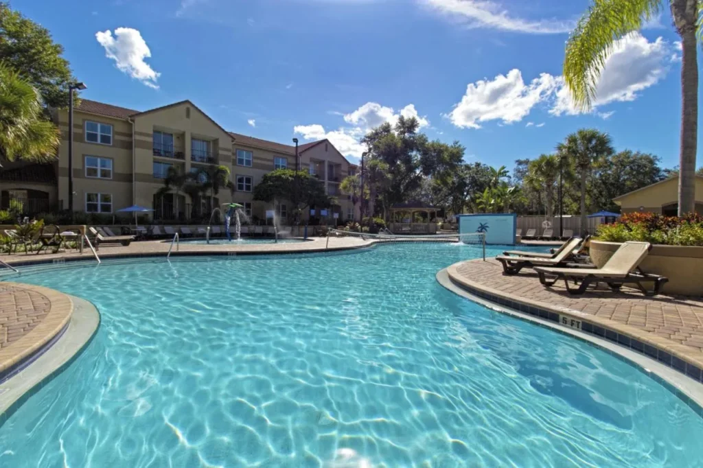 Large outdoor pool with loungers, palm trees and villa buildings at Westgate Blue Tree Resort