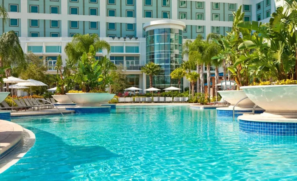 Large turquoise pool with palm planters and loungers in front of the Hilton Orlando hotel tower