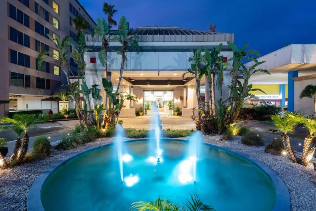 Lit fountain and palm-lined lobby entrance at dusk at Ramada by Wyndham Kissimmee Gateway