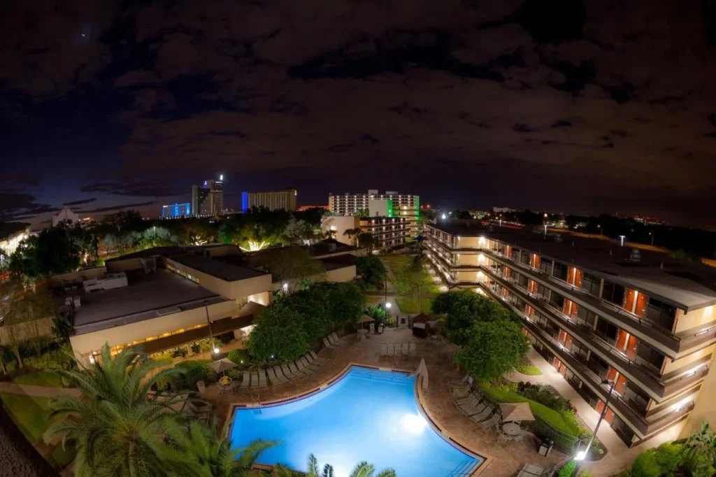 Piscina exterior iluminada y Courtyard por la noche entre las alas de la habitación de Rosen Inn at Pointe Orlando