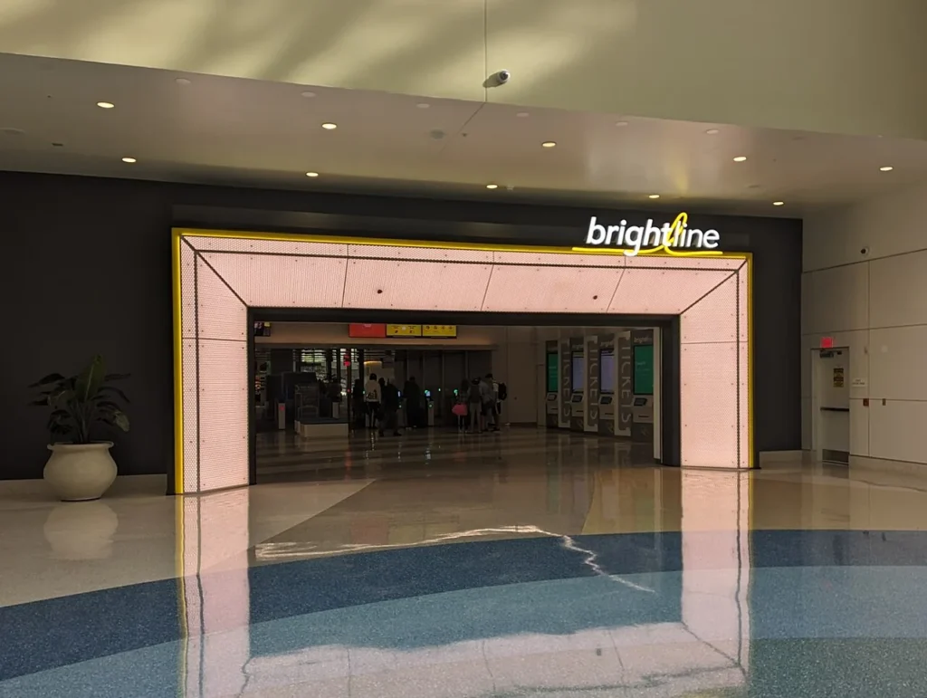 Lit yellow-framed entrance and ticket machines of the Brightline Orlando Station inside the airport train station
