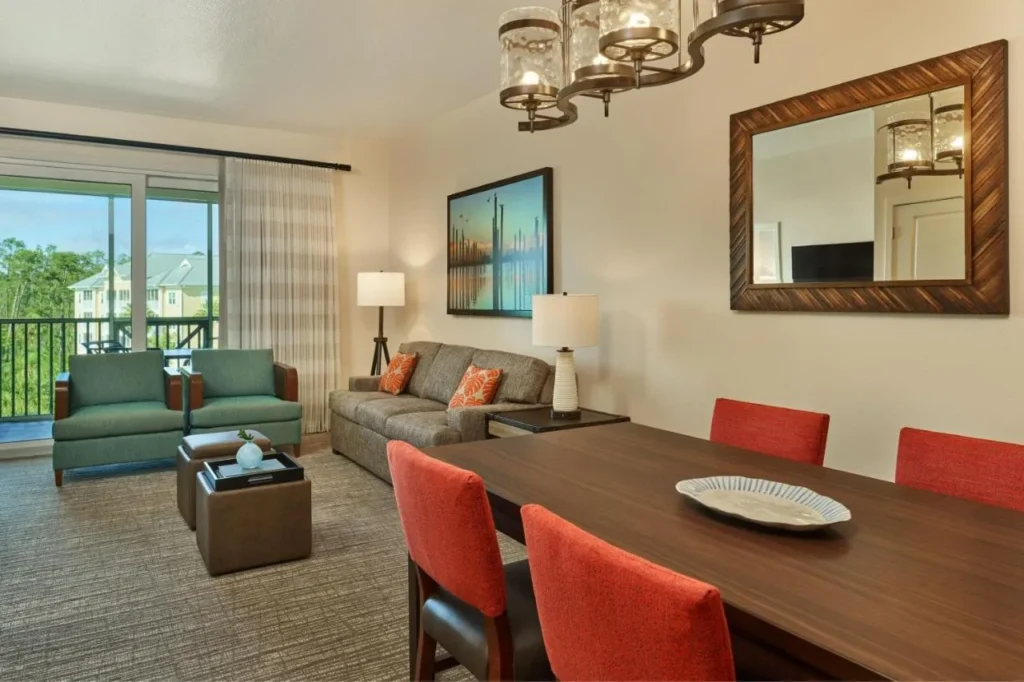 Sala de estar y comedor con sof&aacute;, sillas de comedor rojas y vista al balc&oacute;n en Sheraton Vistana Villages