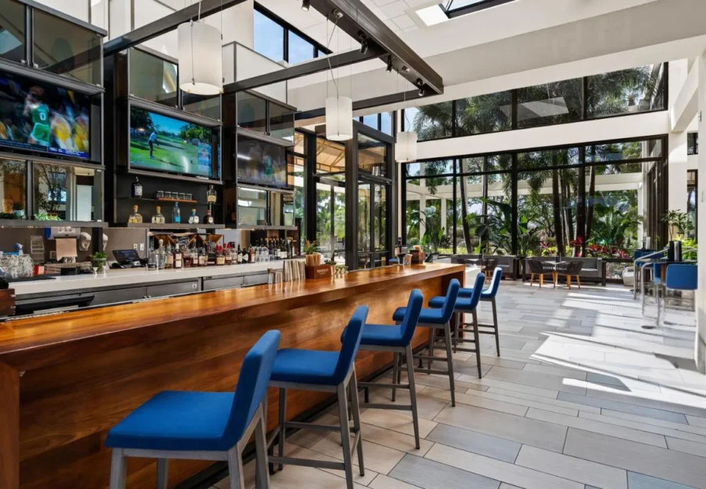 Barra de vestíbulo del Hyatt Regency Grand Cypress con taburetes azules, mostrador de madera, televisores y ventanas altas en el atrio