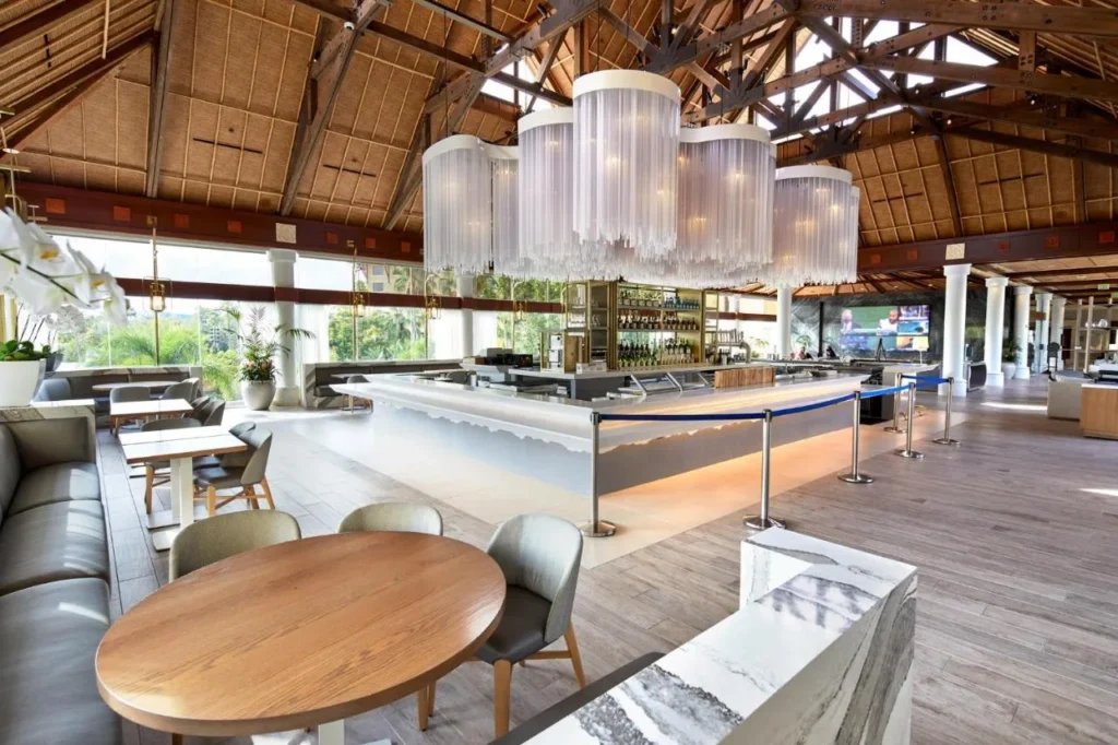 Bar en el vest&iacute;bulo bajo un techo tejido y una l&aacute;mpara de ara&ntilde;a con franjas de vidrio en Loews Royal Pacific Resort