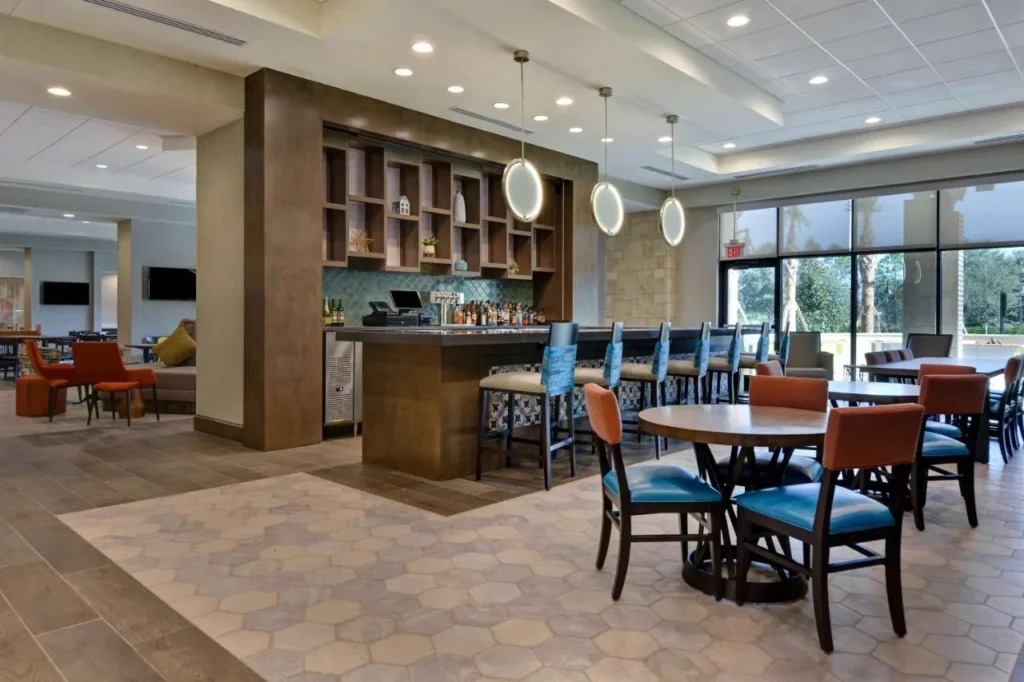 Bar en el vestíbulo con taburetes azules y mesas de comedor en Home2 Suites Orlando Flamingo Crossings