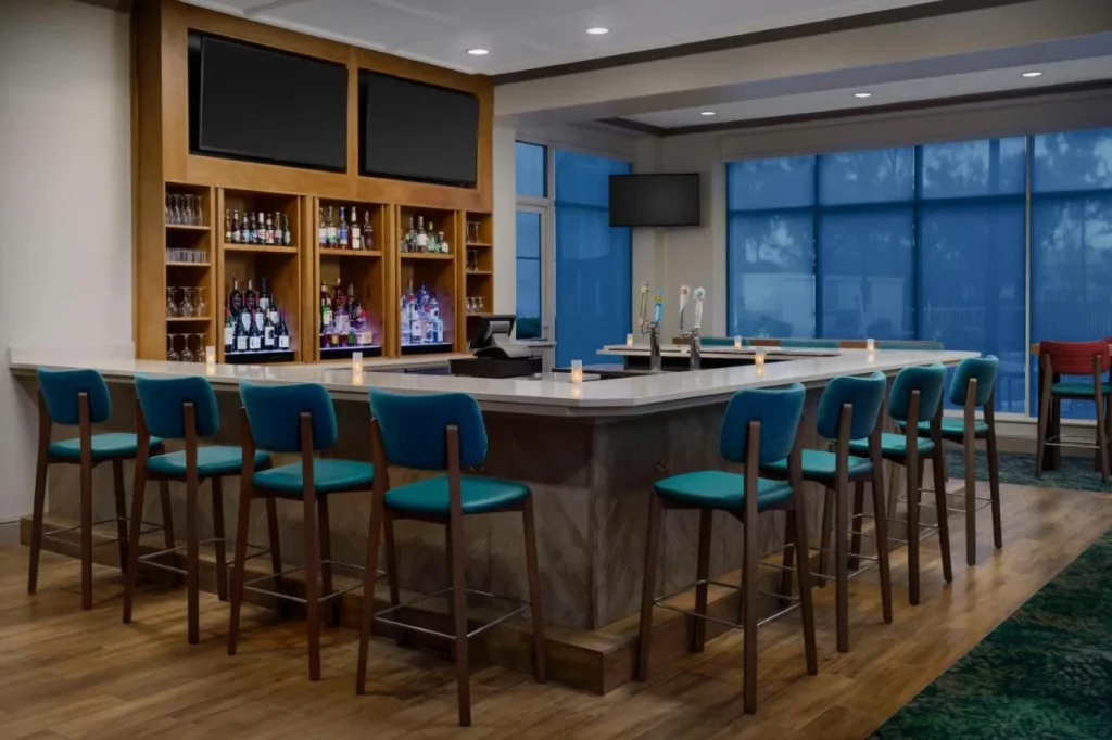 Bar en el vestíbulo con taburetes de color verde azulado y pantallas de televisión en Hilton Garden Inn Orlando at SeaWorld