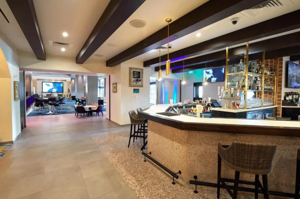 Lobby bar con taburetes tejidos, estantes de botellas iluminados y un sal&oacute;n m&aacute;s all&aacute; en Hard Rock Hotel