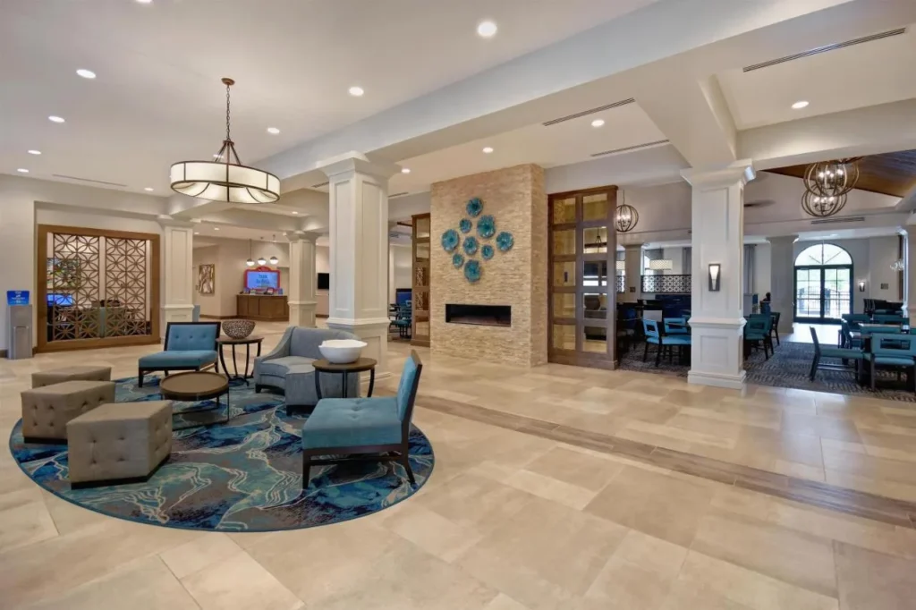 Lobby lounge with blue armchairs, fireplace wall and breakfast area at Homewood Suites Flamingo Crossings