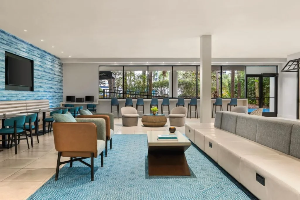 Lobby lounge with blue rug, armchairs and pool-view windows at Delta Hotels Orlando Celebration